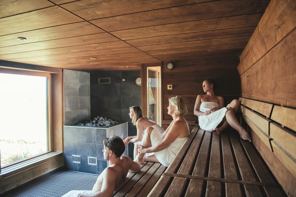 Besucher sitzen entspannt in der Sauna und blicken aus einem bodentiefen Fenster.